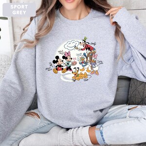 May include: Sport grey sweatshirt featuring a colorful graphic of Disney characters, including Mickey Mouse, Minnie Mouse, Donald Duck, and Goofy. The design includes the characters' names and a heart symbol. The sweatshirt is a crew neck style.
