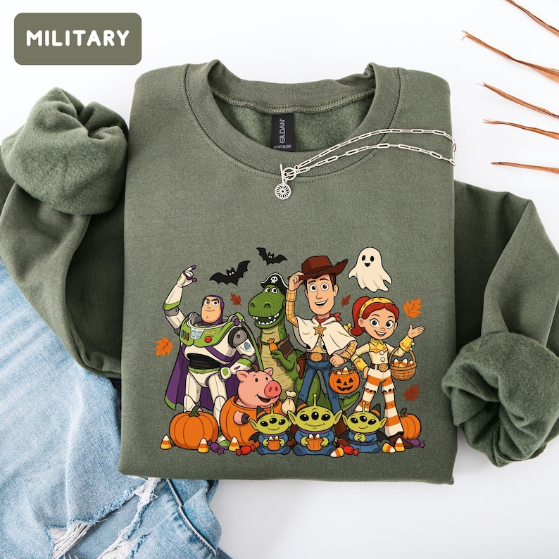 Puede incluir: Una sudadera de cuello redondo color verde militar con un estampado gr&aacute;fico de personajes de Toy Story disfrazados de Halloween, incluyendo a Buzz Lightyear, Woody, Jessie, Rex, Hamm y tres alien&iacute;genas, rodeados de calabazas, murci&eacute;lagos y un fantasma.