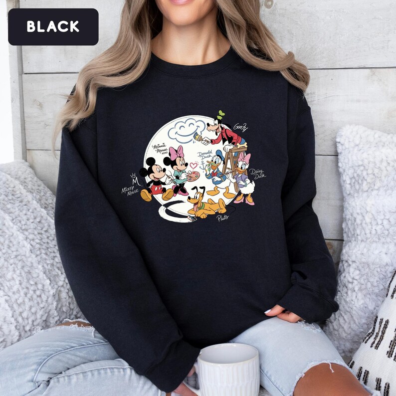 May include: Black crewneck sweatshirt featuring a colorful graphic of Disney characters, including Mickey and Minnie Mouse, Donald and Daisy Duck, Goofy, and Pluto. The design is set against a white cloud background. The word "Black" is in the upper left corner.