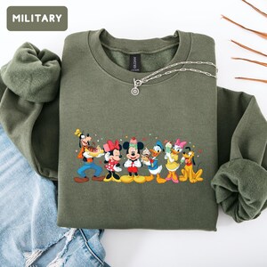 May include: A military green crewneck sweatshirt featuring a graphic print of Disney characters including Goofy, Minnie Mouse, Mickey Mouse, Donald Duck, Daisy Duck, and Pluto holding various ice cream treats. The text MILITARY appears in a box.