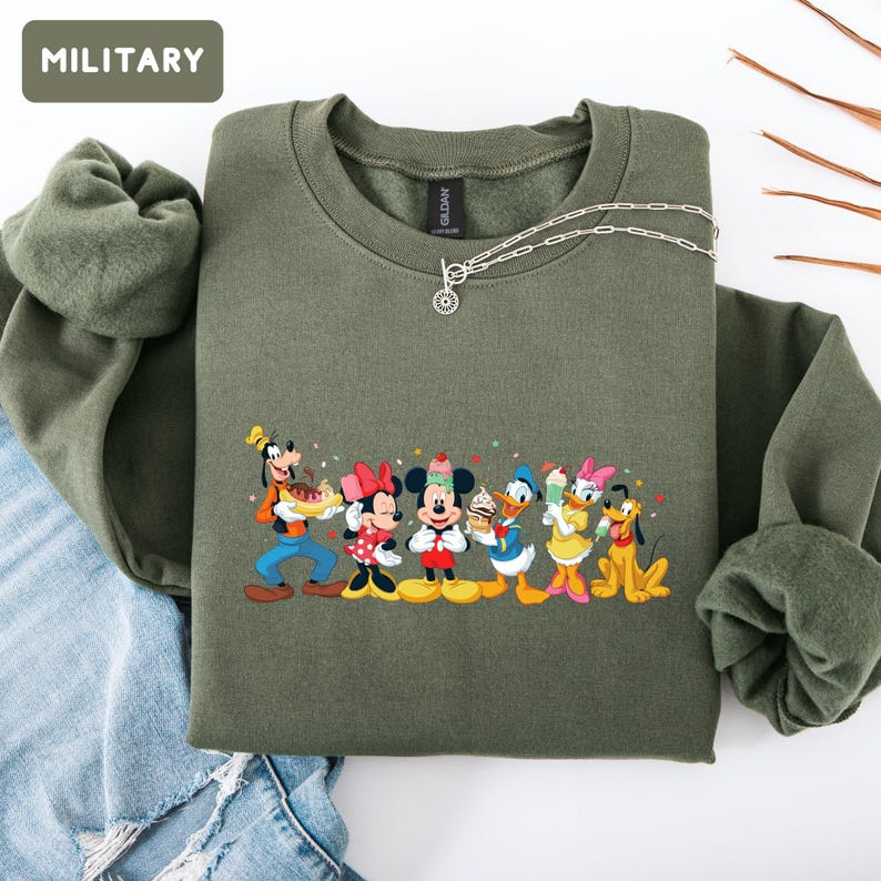 May include: A military green crewneck sweatshirt featuring a graphic print of Disney characters including Goofy, Minnie Mouse, Mickey Mouse, Donald Duck, Daisy Duck, and Pluto holding various ice cream treats. The text MILITARY appears in a box.
