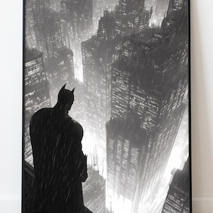 Könnte beinhalten: Ein schwarz-weiß gerahmter Kunstdruck, der die Silhouette einer Figur mit Umhang auf einem hohen Vorsprung über einer regnerischen, dichten Skyline bei Nacht zeigt. Die Szene umfasst hohe Wolkenkratzer mit beleuchteten Fenstern und Regen.
