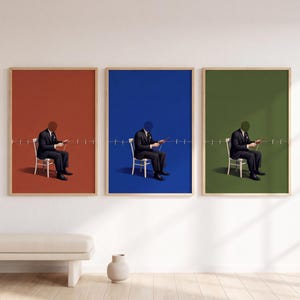 May include: A set of three framed wall art prints featuring a person in a dark suit sitting on a white chair. Each print has a solid background in rust orange, royal blue, or olive green, with a horizontal line of clothespins across the center.
