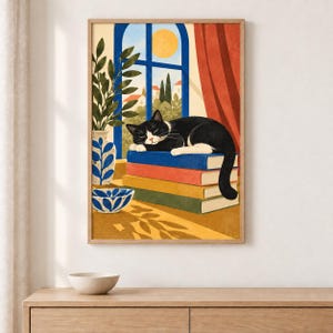 Könnte beinhalten: Ein gerahmter Kunstdruck, der eine schwarz-weiße Katze zeigt, die auf einem Stapel aus drei bunten Büchern schläft. Neben den Büchern stehen eine blau-weiß gemusterte Vase und eine passende Schale. Ein Fenster zeigt eine gelbe Sonne und Bäume.