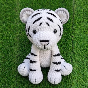 May include: A white tiger plush toy with black stripes and grey accents. The soft toy has a textured appearance and is sitting upright on a green surface. The tiger has black eyes and a black nose. A handmade item.
