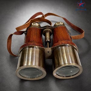 May include: Binoculars featuring a polished brass finish on the objective lens barrels and a wood-grain texture on the main body. The device includes a central brass focusing knob and a brown leather neck strap attached to the sides.