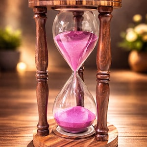 Könnte beinhalten: Holz-Sanduhr mit einer transparenten Glaskammer, die mit rosa Sand gefüllt ist. Die Sanduhr wird von einem Holzrahmen und einer Basis getragen. Das Wort "JUPITER" ist in der oberen linken Ecke sichtbar.