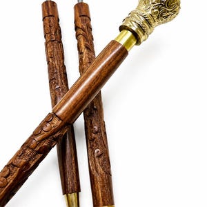 Könnte beinhalten: Ein dreiteiliger Gehstock mit einem dunkelbraunen, geschnitzten Holzschaft mit komplexen Blumenmustern. Der Griff besteht aus poliertem, goldfarbenem Metall mit kunstvollen Prägungen. Die Segmente sind durch Gewindeverbindungen verbunden.