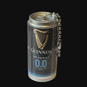 May include: Miniature Guinness Draught 0.0 can keychain. The black and gold can features the Guinness logo and harp, with the text "DRAUGHT 0.0 ALCOHOL FREE STOUT". The keychain has a silver ball chain and clasp.