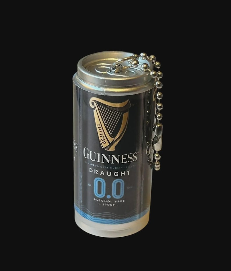 May include: Miniature Guinness Draught 0.0 can keychain. The black and gold can features the Guinness logo and harp, with the text "DRAUGHT 0.0 ALCOHOL FREE STOUT". The keychain has a silver ball chain and clasp.