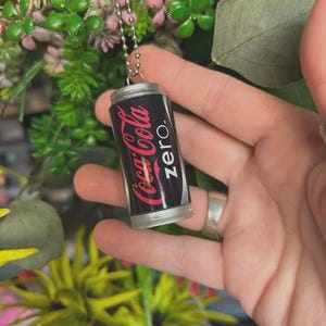 Peut inclure: Pendentif miniature en forme de canette Coca-Cola Zero. Le haut et le bas sont argentés. La canette noire porte le logo Coca-Cola en rouge et le mot « zero » en blanc. Suspendu à une chaîne à billes argentée.
