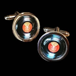 May include: Silver cufflinks with a retro vinyl record design. The records are black with red and orange labels. The cufflinks are set against a black backdrop, showcasing a classic music theme.