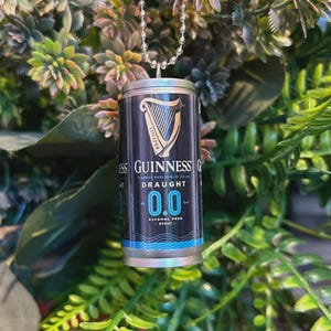 May include: A miniature Guinness Draught 0.0 can pendant. The black and silver can features the Guinness logo, a harp, and the words "Draught 0.0 Alcohol Free Stout". The pendant hangs from a silver ball chain.