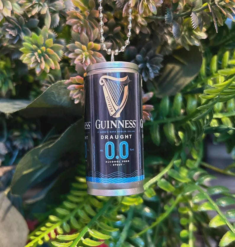 May include: A miniature Guinness Draught 0.0 can pendant. The black and silver can features the Guinness logo, a harp, and the words "Draught 0.0 Alcohol Free Stout". The pendant hangs from a silver ball chain.