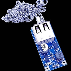 May include: A silver-toned metal chain necklace featuring a rectangular blue circuit board pendant. The pendant includes a silver USB port, a cylindrical capacitor labeled 100 16V VT, and various small electronic components soldered onto the board.