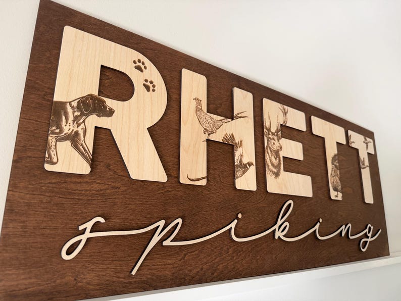 May include: Wooden sign with the name "Rhett" in large, light-colored letters, each featuring a different animal illustration. The name "Spiking" is written in a cursive font below. The background is a dark brown.
