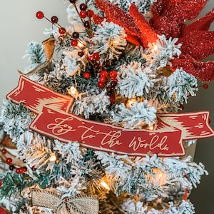 May include: A flocked Christmas tree decorated with red berries, a red felt poinsettia, and a red banner with the text "Joy to the World".