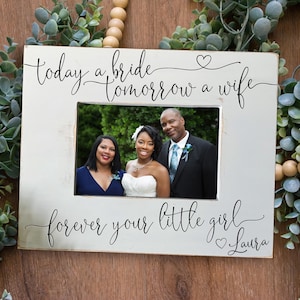 Peut inclure: Cadre photo en bois blanc avec le texte "today a bride tomorrow a wife forever your little girl Laura" et une photo d'une mariée et d'un marié avec une femme debout à côté d'eux.