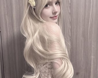 May include: A long, wavy, platinum blonde wig with bangs and a small, yellow, dog-shaped hair clip attached to the side. The hair has a soft, voluminous texture with loose curls cascading down the back, styled in a layered, shoulder-length cut.