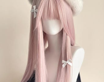 Könnte beinhalten: Eine lange, glatte, pastellrosa Perücke mit Pony, präsentiert auf einem weißen Schaufensterpuppenkopf. Die Perücke ist mit einem flauschigen weißen Barett und zwei kleinen, weißen Schleifen an den Haarsträhnen beidseitig verziert.