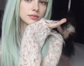 Könnte beinhalten: Eine lange, glatte, mintgrüne Perücke mit Pony, kombiniert mit einem grob gestrickten, cremefarbenen Pullover mit dezenten braunen und orangefarbenen Sprenkeln im gesamten Stoff. Der Pullover hat ein lockeres, strukturiertes Gewebe und lange Ärmel.