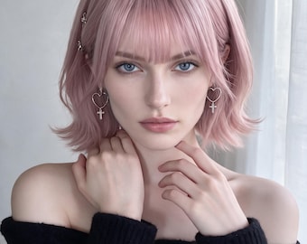 Könnte beinhalten: Eine schulterlange, pastellrosa Perücke mit geradem Pony und leicht nach außen geschwungenen Spitzen. Das Haar ist mit einer kleinen silbernen Haarspange auf der rechten Seite und silbernen herzförmigen Ohrringen mit Kreuzanhängern versehen.