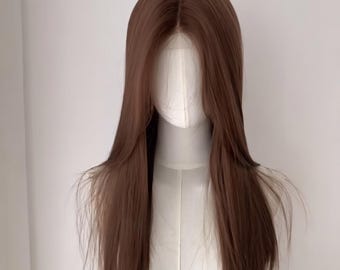 Può includere: Una parrucca lunga e liscia color marrone medio con riga centrale e ciocche scalate che incorniciano il viso. I capelli hanno una consistenza liscia e poggiano su una testa di manichino bianca, mostrando un'attaccatura frontale in pizzo.