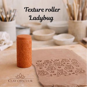 Peut inclure: Un rouleau à texture en argile de couleur terre cuite avec un motif répétitif de coccinelles et de cœurs. Le rouleau est placé à côté d'une plaque d'argile plate présentant le motif gaufré. Le texte indique Texture roller Ladybug et CLAY OBSCUUR.