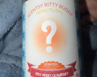 Scentsy Bitty Buddy in Very Merry Cranberry fragrance. White container with red label accents and blue patterned sides. Compact scented acce