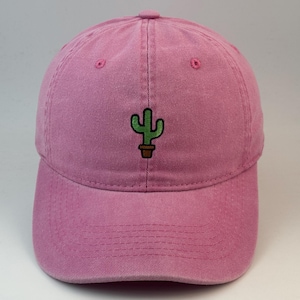 May include: A pink baseball cap featuring an embroidered green cactus in a brown pot centred on the front panel. The cap has a curved brim, a button on the top, and stitched eyelets for ventilation, providing a simple and clean aesthetic.