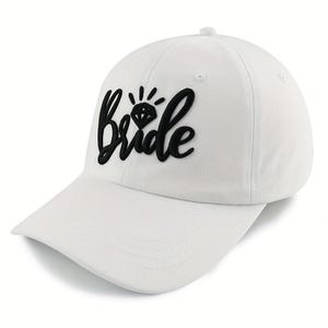 Könnte beinhalten: Eine weiße Baseballkappe mit dem Wort bride in erhabener schwarzer Schrift auf der Vorderseite. Über dem Buchstaben i befindet sich eine kleine schwarze Grafik eines Diamanten mit strahlenförmigen Linien. Die Kappe hat eine feste Form.