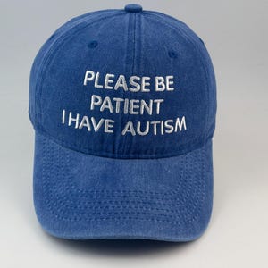 以下が含まれることがあります： PLEASE BE PATIENT I HAVE AUTISMという白い刺繍文字がフロントに入った、ブルーのウォッシュ加工生地のベースボールキャップ。キャップにはカーブしたつば、トップのボタン、パネルに沿った目に見えるステッチが施されています。