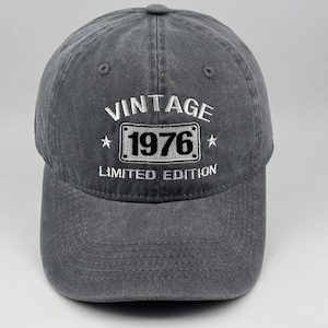 以下が含まれることがあります： VINTAGE 1976 LIMITED EDITIONと白い刺繍が施されたチャコールグレーの野球帽。1976という数字の周りには長方形の枠があり、中央の長方形のグラフィックの両側には小さな星が2つデザインされています。