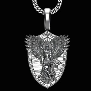 Op de afbeelding: Zilveren hangerketting met een gedetailleerde afbeelding van een engel met uitgespreide vleugels, die een zwaard vasthoudt en boven een slang staat. De hanger is schildvormig en hangt aan een zilveren ketting. Het ontwerp is ingewikkeld en gedetailleerd.