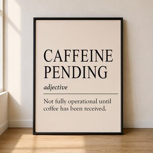 Könnte beinhalten: Ein gerahmter Kunstdruck mit beigem Hintergrund und schwarzem Text. Der Text lautet CAFFEINE PENDING, gefolgt von dem Wort adjective in Kursivschrift, einer horizontalen Linie und der Definition: Not fully operational until coffee has been received.