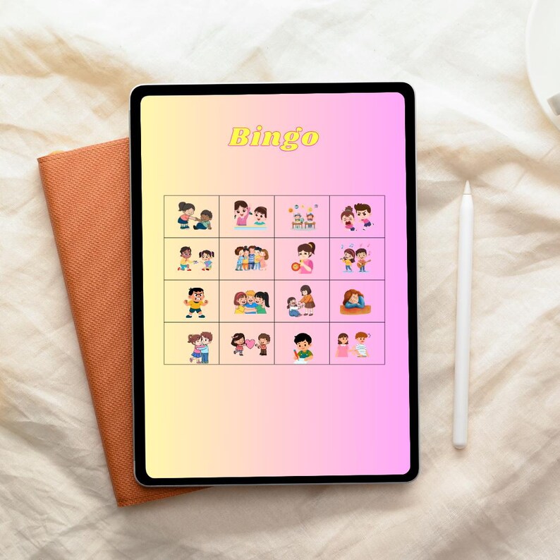 Peut inclure: Une tablette num&eacute;rique affichant un jeu de Bingo avec des illustrations color&eacute;es de personnes. Le mot "Bingo" est &eacute;crit en jaune en haut. Un carnet marron et un stylet blanc sont &agrave; c&ocirc;t&eacute; de la tablette.