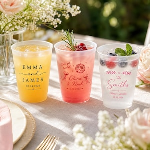 May include: Three clear plastic cups filled with colorful drinks. The first cup has black text reading EMMA and JAMES 05.24.2026. The second cup has red text reading Let's get toasted! Olivia & Noah 11.14.2026. The third cup has pink text reading The Smiths Oliver + Amelia 08.12.2026.