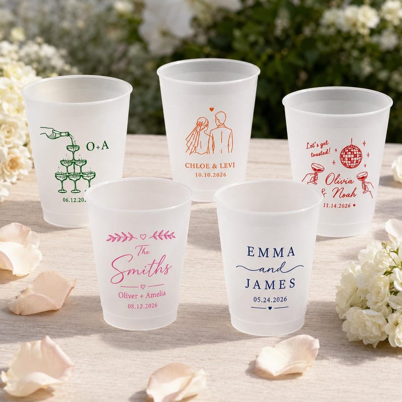 May include: Five frosted plastic cups featuring custom wedding-themed graphics and text. Designs include a champagne tower, a couple, a disco ball with the text Let's get toasted, the name The Smiths, and the names Emma and James with dates.