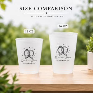 May include: Two frosted plastic cups labeled 12 oz and 16 oz, featuring a black graphic of two interlocking rings with a bow, the text Sarah and James, and the date 07.04.2026. The image includes the text SIZE COMPARISON 12 OZ & 16 OZ FROSTED CUPS.