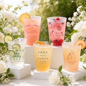 May include: Five clear plastic cups filled with colorful beverages and fruit garnishes. Each cup features custom printed text and graphics, including names and dates, celebrating various couples and wedding dates in a variety of ink colors.