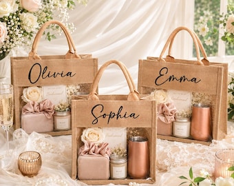 May include: Three jute tote bags with clear panels, each personalised with a name in elegant script. The bags contain gifts like candles, roses, and tumblers. The bags are for a bridesmaid gift set.