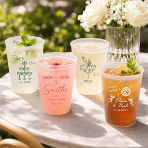 May include: Four clear plastic cups filled with various colored beverages. Each cup features custom printed designs including names, dates, and illustrations like a champagne tower, a couple in a glass, and a disco ball with the text Let's get toasted.