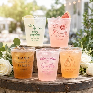 May include: Five clear plastic cups filled with various colored beverages, each featuring custom printed designs. The cups display names, dates, and illustrations including a champagne tower, a disco ball, floral accents, and a couple in wedding attire.