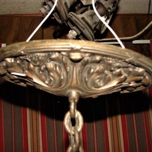 May include: A vintage brass ceiling light fixture with an ornate, detailed design. The fixture has a chain hanging from it and is ready to be installed.