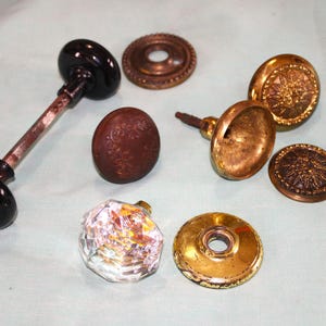 May include: Assortment of vintage door knobs in various styles and materials, including brass, glass, and black metal. Some knobs feature intricate designs.