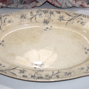 May include: An oval serving platter with a cream-colored base and a floral design in shades of gray. The edges of the platter have a scalloped shape, and the floral pattern is repeated around the rim. A vintage piece.