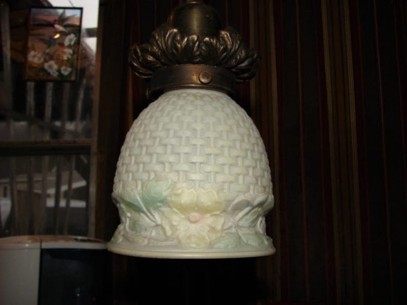 May include: A white glass ceiling light fixture with a woven pattern and floral accents. The fixture has a brass base and a decorative metal trim.