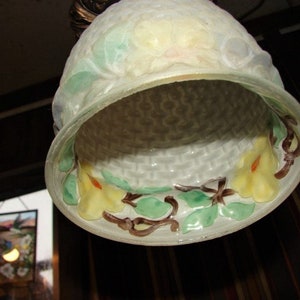 May include: A white glass lampshade with a woven pattern and floral designs in shades of green, yellow, and brown. The lampshade has a scalloped edge and a delicate, feminine aesthetic.