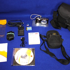 May include: A black Kodak EasyShare digital camera with a wrist strap, a large black camera bag, a smaller black carrying case, a battery, a memory card, a battery charger with a power cord, a USB cable, a software CD, and a Kodak EasyShare manual.