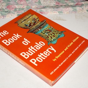 May include: A hardcover book titled "The Book of Buffalo Pottery" with an orange cover. The cover features an illustration of pottery and the text "by Seymour and Violet Altman". The book contains 400 pieces illustrated in color and black and white.